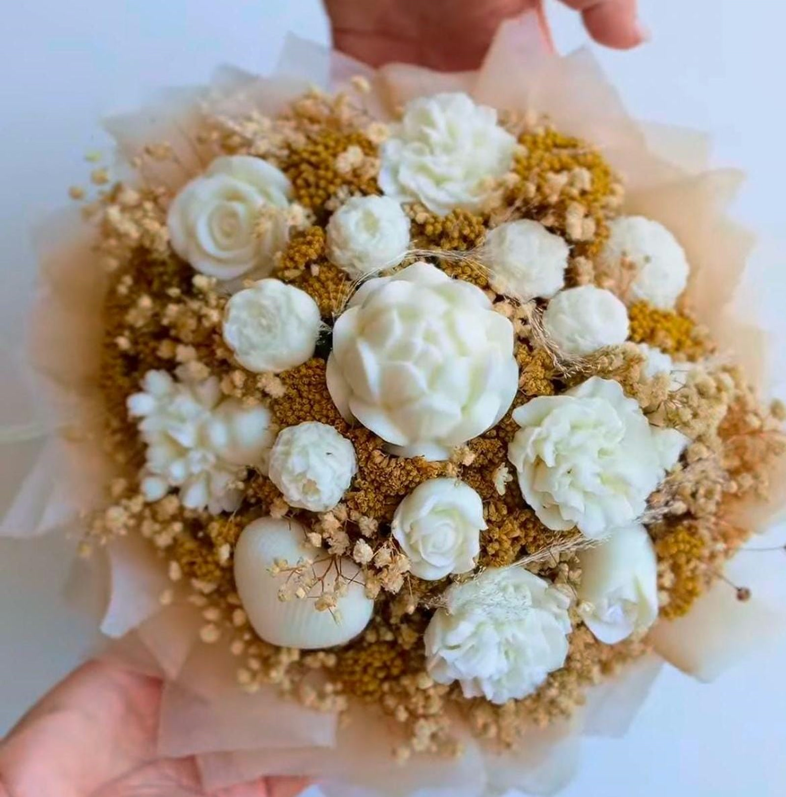 Bouquet di fiori in cera bianca con fiori secchi dorati tenuto tra le mani