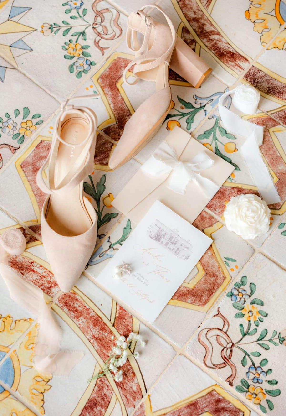 Flatlay di nozze con scarpe cipria, invito e candela a forma di rosa su pavimento in maiolica