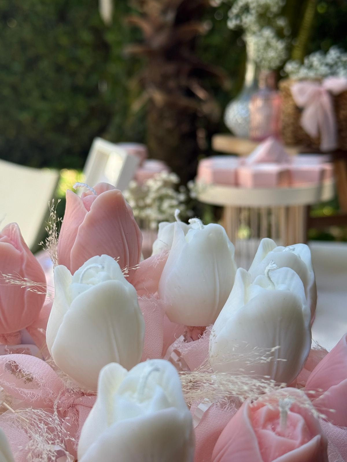 Candele a forma di tulipano in cera di soia, bianche e rosa cipria, su un allestimento con veli e fiori secchi
